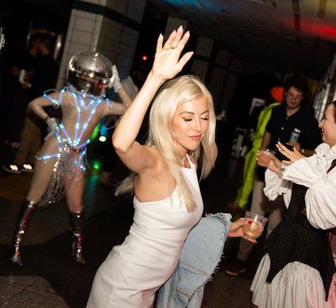 A person wearing a white dress has their hand up in the air as they dance on a dancefloor