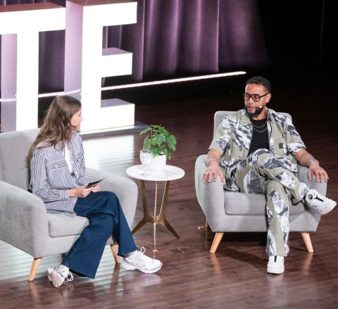 Two people sitting in chairs on a stage talking at a past Elevate Festival
